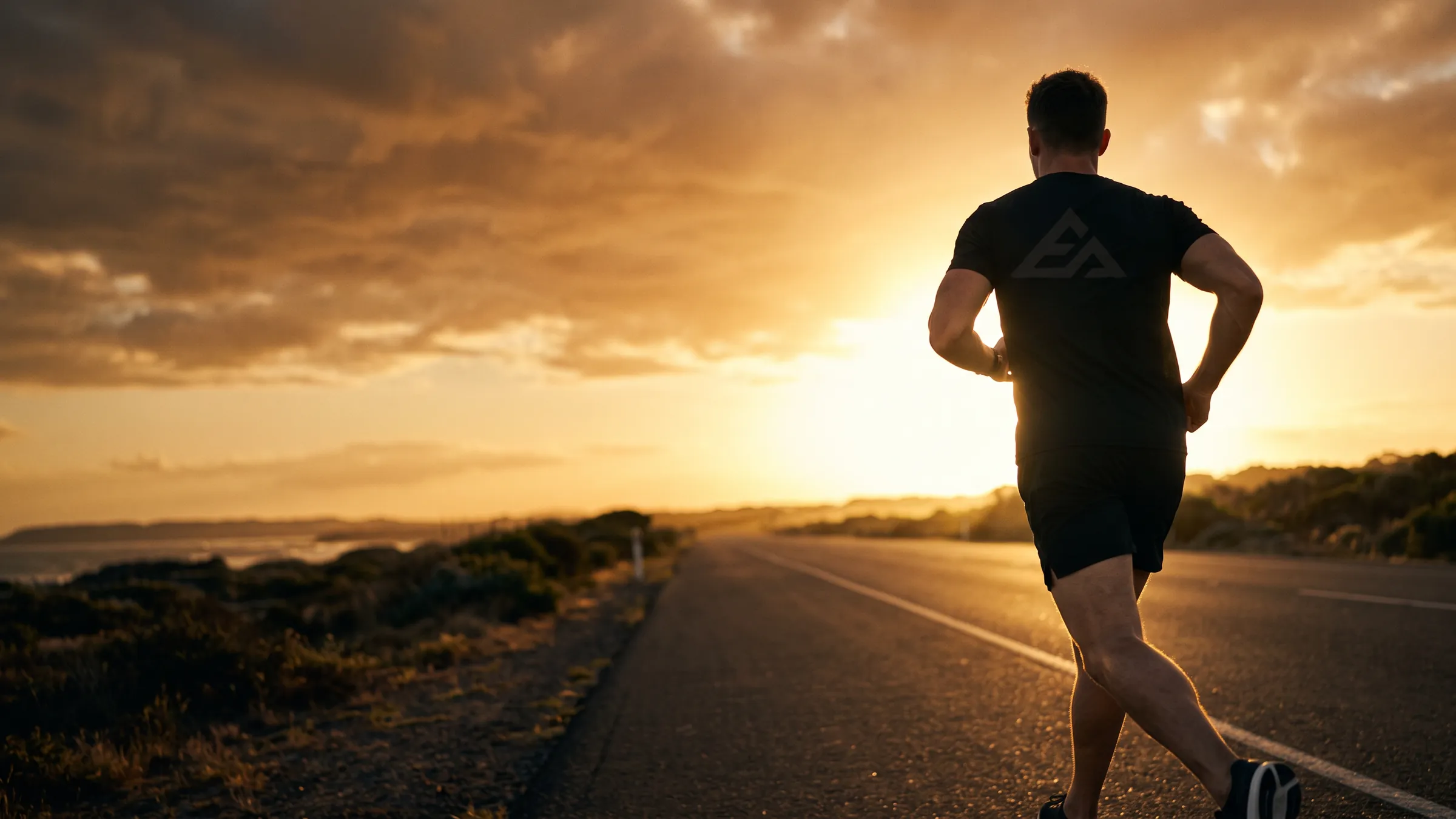 Runner in black training gear on an empty road at sunset